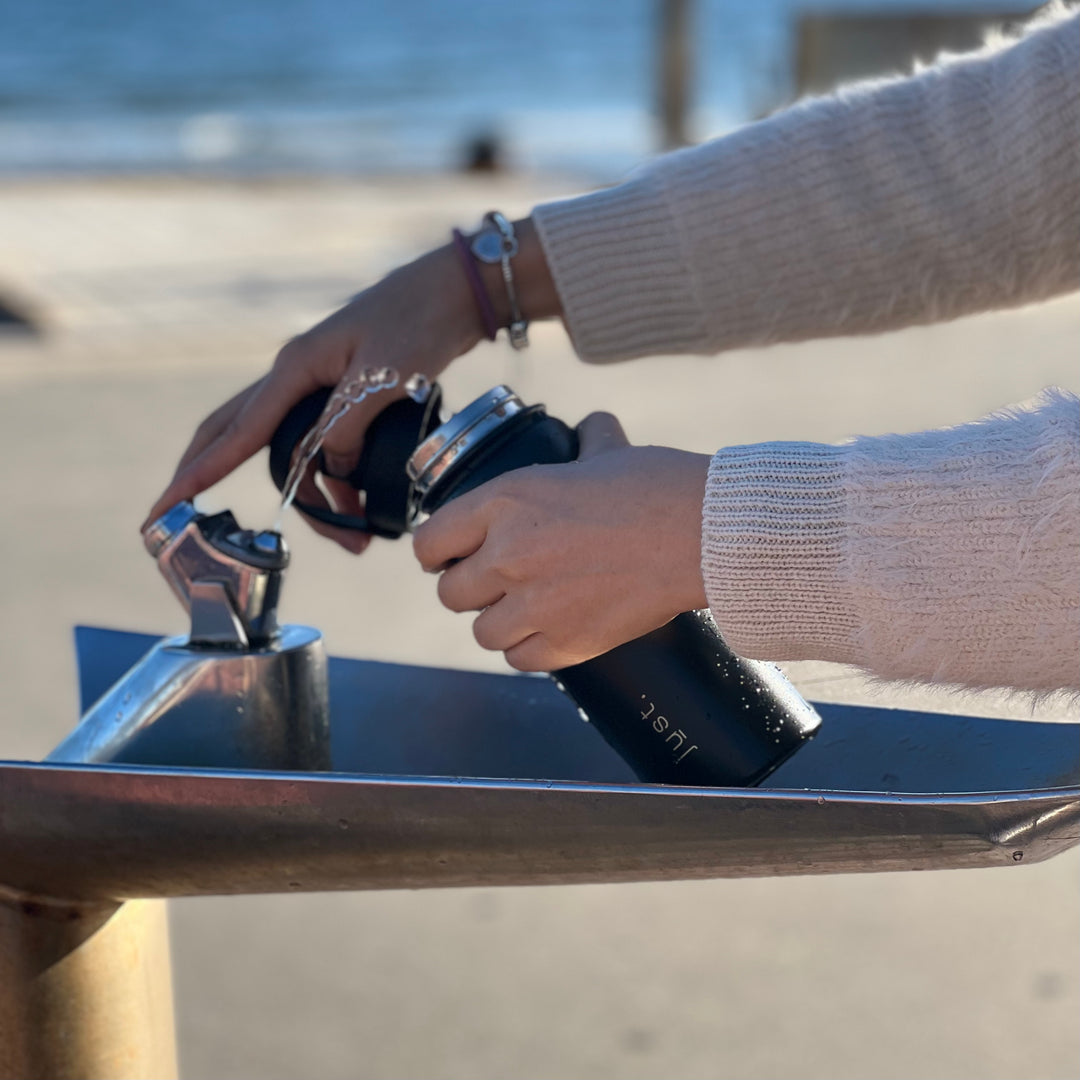 fill water into black stainless steel bottle on the beach
