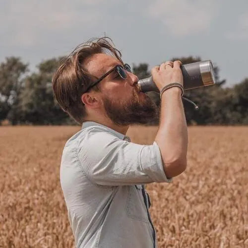 person standing in wheat field drinking from a grey water bottle